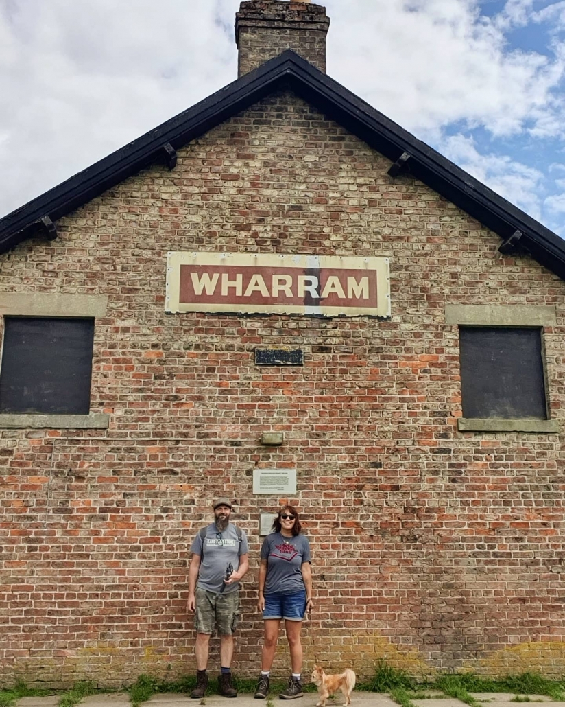 Man and woman in front of a brick building that has the sign saying wharram on it at wharram Percy medieval village